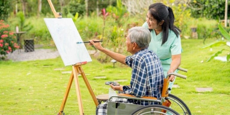 Elderly Man Painting Outdoors at one of the Assisted Living Facilities in Katy TX with the Guidance of His Skilled Nurse