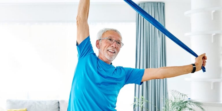 Elderly Man Stretching with a Resistance Band Inside a Bright Room at an Assisted Living Facility
