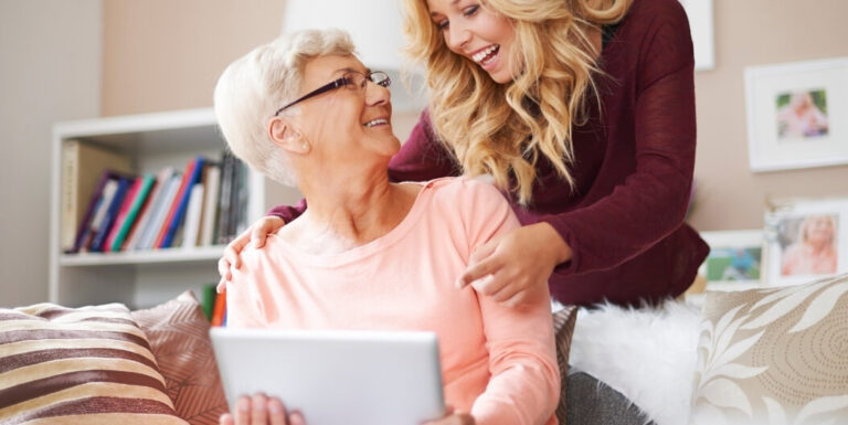 Granddaughter Sharing Photos on a Tablet with Elderly Woman at Memory Care Facility